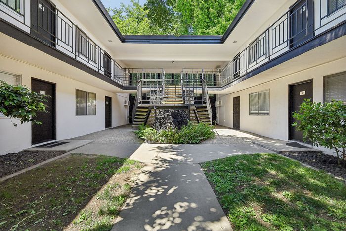 Charming apartment courtyard with lush greenery, modern stairway, and stylish exterior design.
