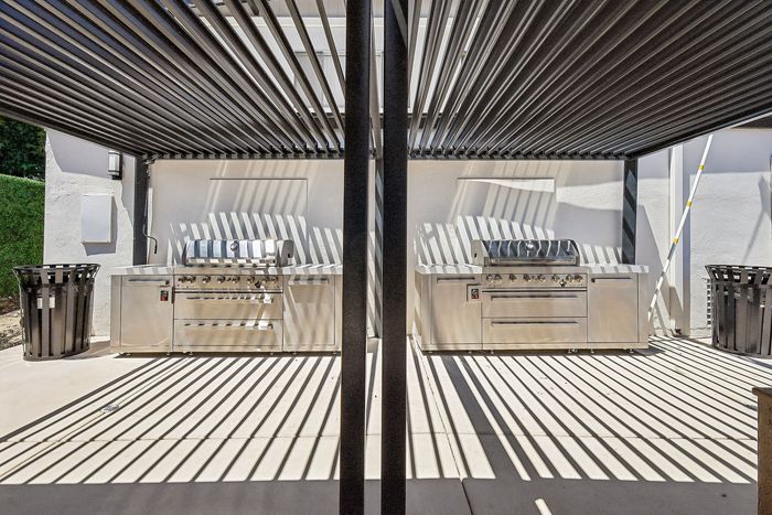 Modern outdoor kitchen with sleek stainless steel grills, under a stylish pergola casting artistic shadows.