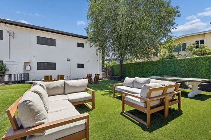 Charming outdoor space with cozy cushioned seating, lush green lawn, and beautiful mature trees, perfect for relaxation and entertaining.