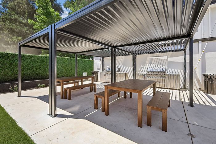 Chic outdoor dining area with modern pergola and barbecue grills, surrounded by lush greenery for stylish living and entertaining.