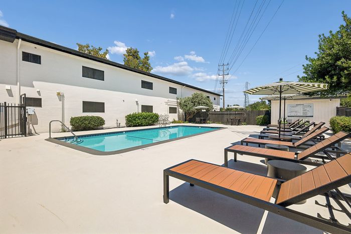 Inviting apartment pool area with modern sun loungers and stylish umbrellas, perfect for relaxation and sunny afternoons.