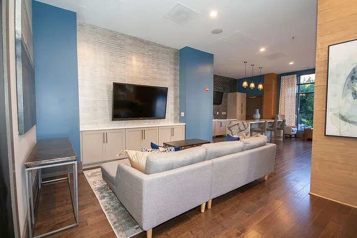 Modern living room with sleek gray sofa, large flat-screen TV, and dining area, featuring stylish pendant lights and expansive windows for natural light.