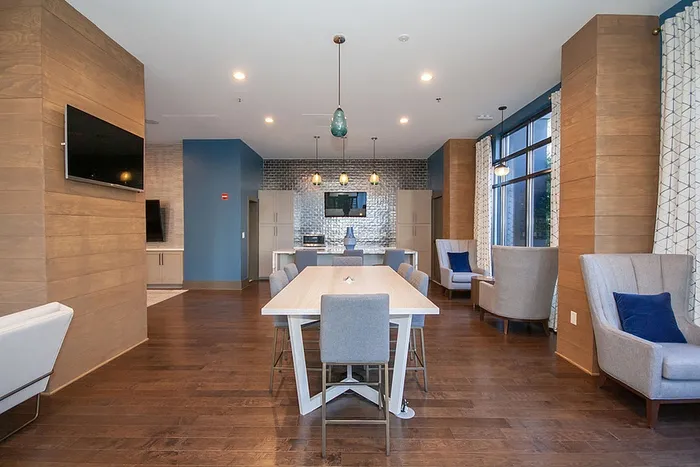 Elegant communal lounge featuring a modern dining table, cozy seating, and a kitchenette with ambient lighting, ideal for gatherings.