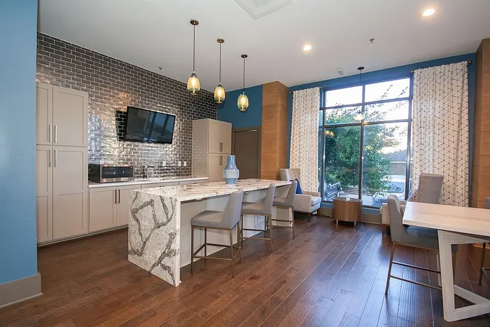 Modern kitchen with elegant gray cabinetry, sleek marble island, and cozy seating area, bathed in natural light from large windows.