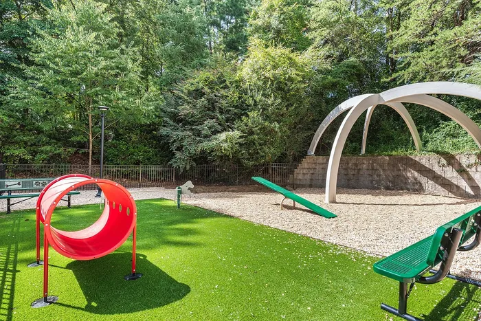 Charming playground with vibrant red tunnel slide, green seesaw, and lush greenery, perfect for family fun.
