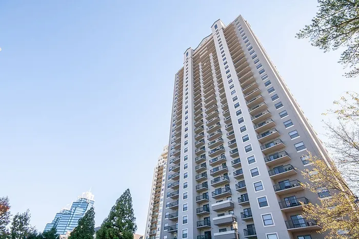 Impressive high-rise apartment building with modern balconies and a stunning cityscape backdrop under a clear blue sky.