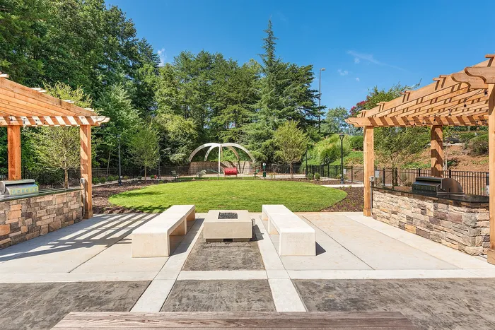 Charming outdoor patio featuring elegant stone benches, a stylish fire pit, and rustic wooden pergolas, surrounded by lush greenery and vibrant trees.