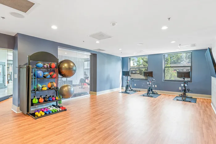 Bright and modern fitness room featuring exercise bikes, colorful kettlebells, and large stability balls on sleek laminate flooring.