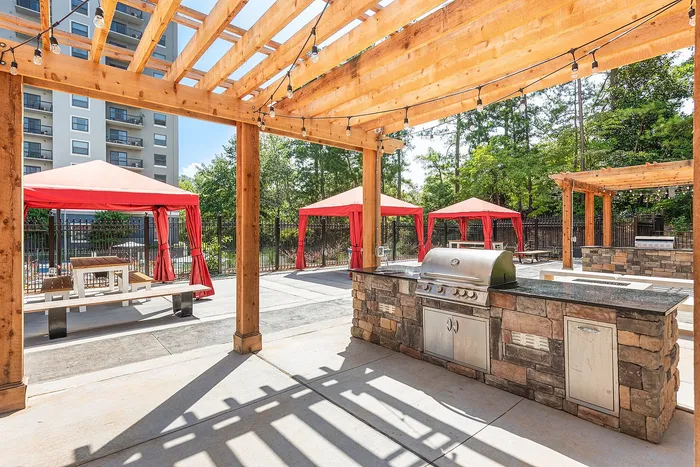 Charming outdoor patio with elegant pergola, featuring a modern grill station and vibrant red cabanas, perfect for entertaining and relaxation.