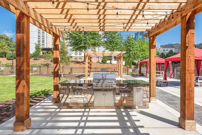 Inviting outdoor patio with a stylish pergola, modern grill station, and vibrant red canopies, perfect for entertaining in a serene setting.