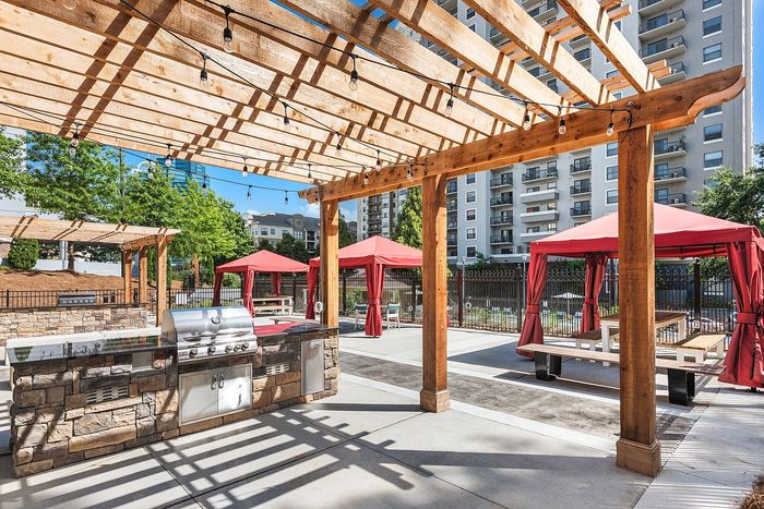 Chic outdoor patio space featuring a stylish pergola, modern stone grill, and inviting red canopies, perfect for entertaining.