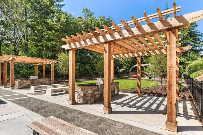 Charming outdoor space with wooden pergolas and built-in grills, surrounded by lush greenery, perfect for entertaining.