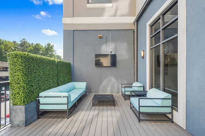 Elegant outdoor terrace with modern seating, a wall-mounted TV, and lush greenery, perfect for entertaining and relaxation.