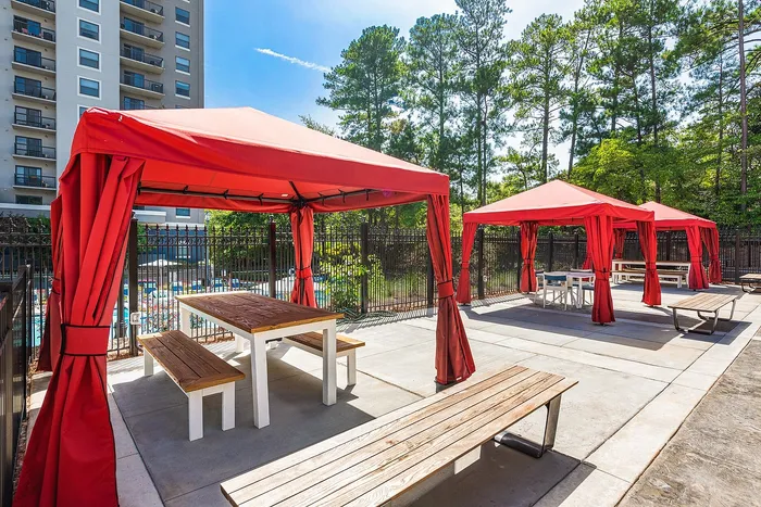 Inviting outdoor space with vibrant red cabanas and wooden picnic tables, perfect for sunny relaxation next to the pool area.