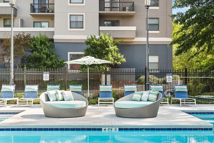 Luxurious apartment outdoor pool area featuring stylish round lounge chairs, vibrant sun umbrellas, and comfortable sunbeds, perfect for relaxation.