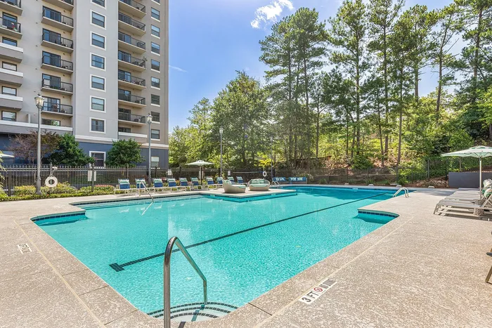 Inviting swimming pool with sun loungers, surrounded by lush greenery and a modern apartment building.