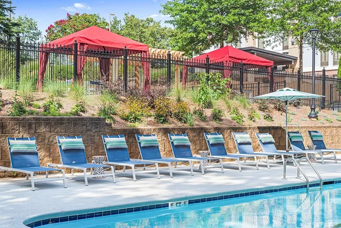Inviting poolside retreat with chic lounge chairs and vibrant red gazebos set in lush garden surroundings.