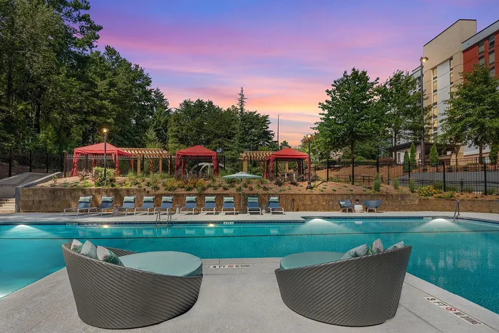 Luxurious resort-style pool area with elegant lounge chairs and cabanas against a stunning sunset backdrop, surrounded by lush greenery.