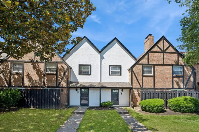 Charming townhouse with Tudor-style brickwork, featuring manicured lawns and inviting entrance under a clear blue sky.