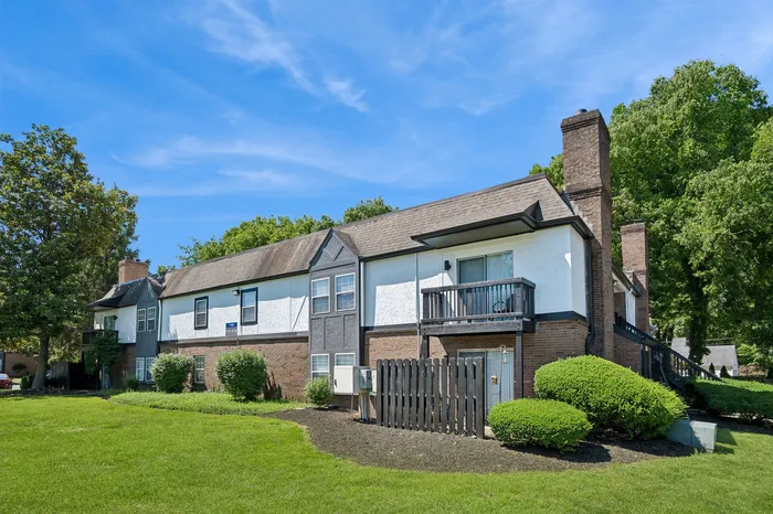 Charming two-story apartment complex with classic brick exterior, surrounded by lush greenery and set against a clear blue sky.