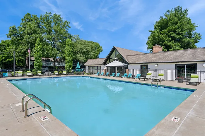 Inviting outdoor pool area with relaxing sun loungers, vibrant greenery, and a charming clubhouse under a bright blue sky.