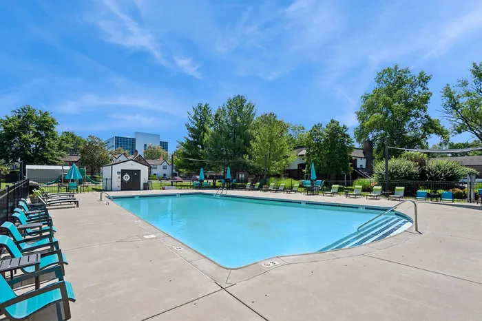 Inviting outdoor pool area with lounge chairs and vibrant umbrellas, surrounded by lush greenery and modern architecture under a bright blue sky.