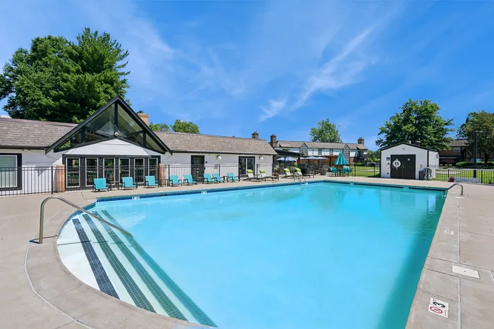 Inviting community pool area with bright blue water, surrounded by lounge chairs and a modern clubhouse, set against a clear blue sky.
