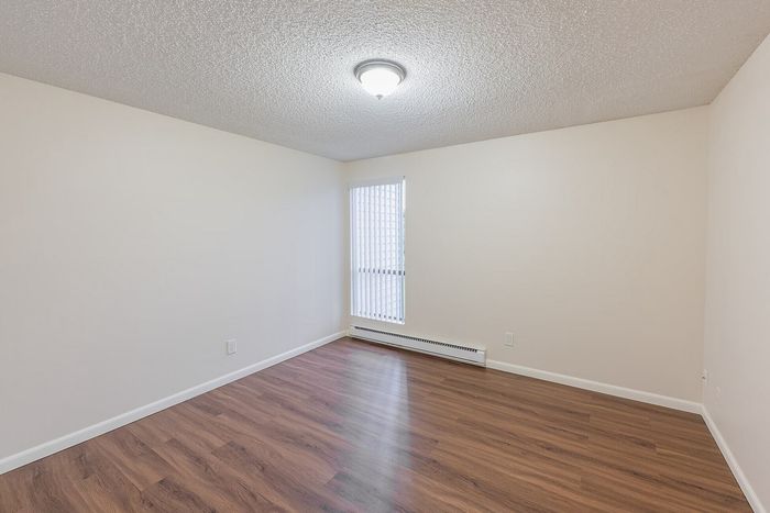Bright empty room with elegant wood flooring and a large window with vertical blinds, perfect for customization.