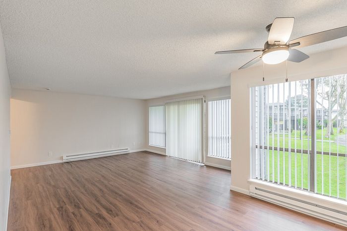 Bright, spacious living room with modern ceiling fan, large windows, and elegant wood flooring, offering serene garden views.
