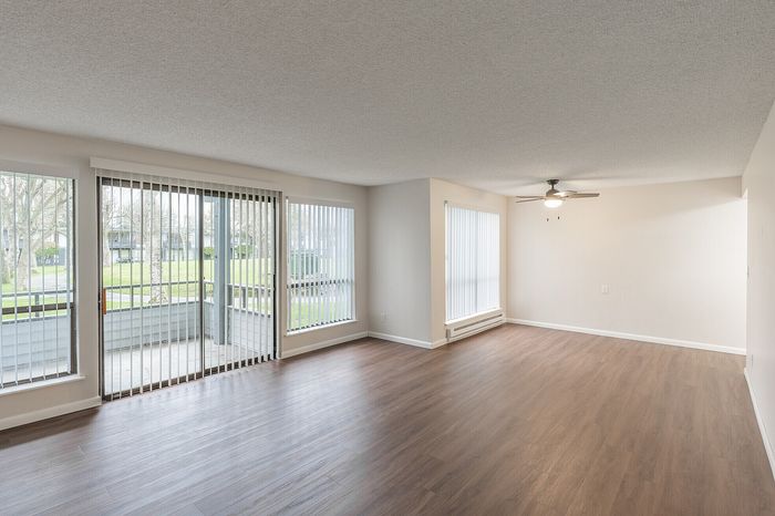 Bright and spacious living area with large windows, modern wood flooring, and a stylish ceiling fan, perfect for comfortable living.