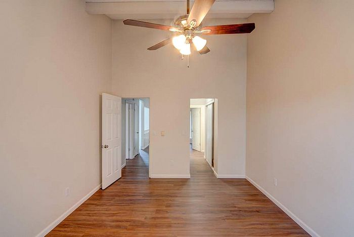 Elegant room with polished wood flooring, high ceiling, and a stylish ceiling fan, leading to a cozy hallway.
