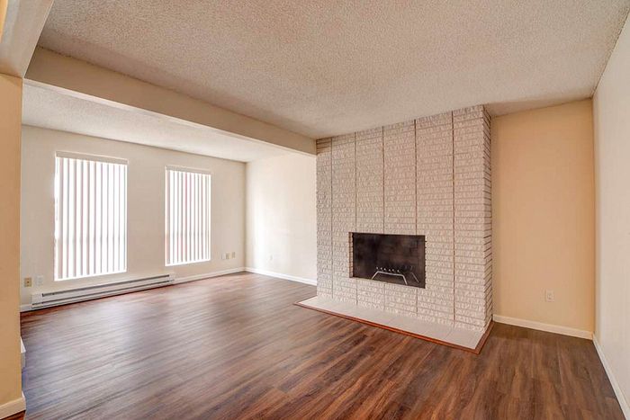 Inviting living room with elegant wood flooring, a stylish brick fireplace, and large windows allowing natural light to illuminate the space.