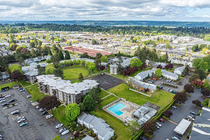 Scenic aerial view of a vibrant apartment community with lush greenery, a central courtyard, tennis court, and a sparkling outdoor pool.