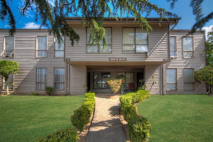 Charming two-story apartment building surrounded by lush greenery and vibrant blue skies.