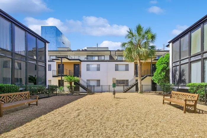 Charming apartment courtyard with palm trees, garden benches, and modern architecture under a vibrant blue sky.