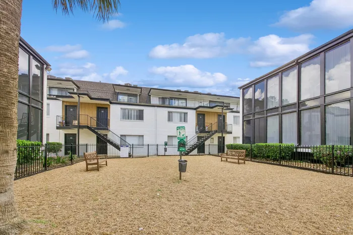 Charming apartment complex featuring a serene courtyard with benches, surrounded by modern architecture and lush greenery under a vibrant blue sky.
