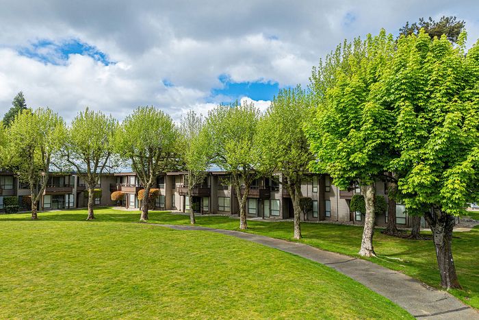 Charming apartment complex surrounded by lush green trees and a spacious lawn, offering serene living with nature views.