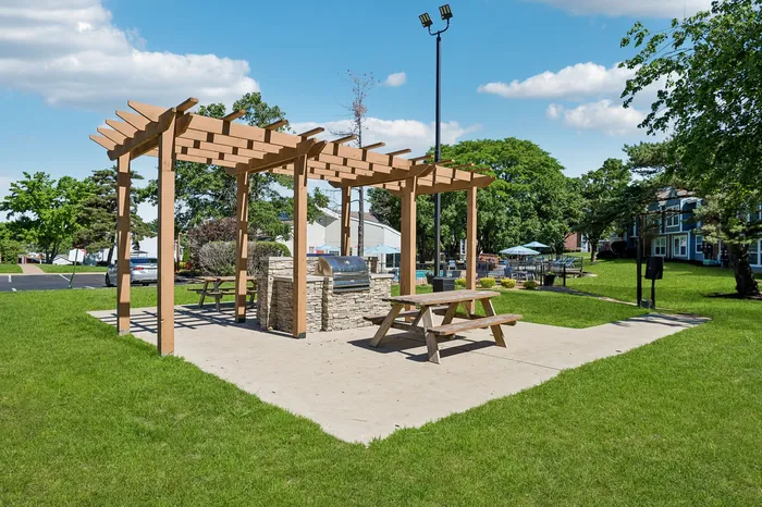 Charming outdoor picnic area with a pergola and barbecue grill, set amidst lush green lawns and vibrant landscaping.