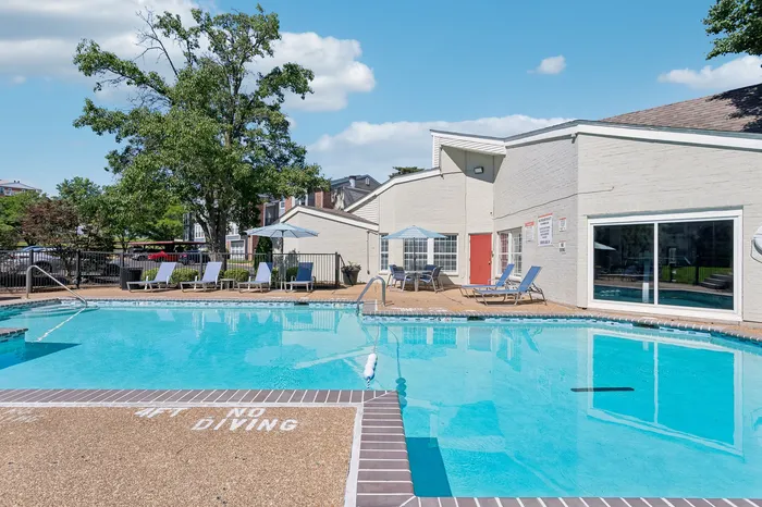 Inviting outdoor pool area surrounded by comfortable lounge chairs and umbrellas, with modern building backdrop and lush greenery.
