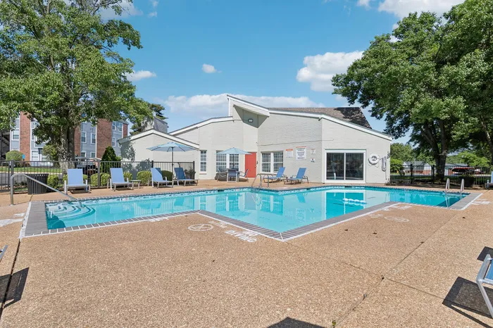 Inviting outdoor pool area with modern lounge chairs and umbrellas, surrounded by lush greenery and bright blue skies.