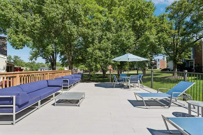 Luxurious outdoor patio with stylish blue lounge chairs, tables with umbrellas, and lush green trees creating a serene, inviting atmosphere.