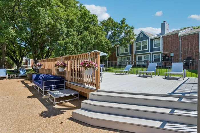 Inviting outdoor deck with modern seating, surrounded by lush green trees and charming residential buildings.