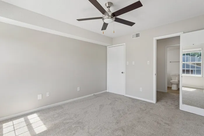 Bright and airy room with plush carpeting, modern ceiling fan, and mirrored closet, leading to an en-suite bathroom.