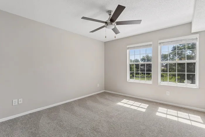 Bright bedroom with large windows, plush carpet, and a ceiling fan, offering serene views.