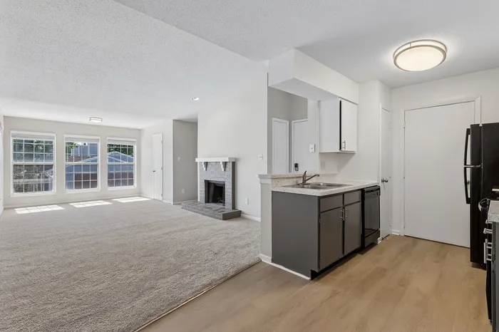 Bright and airy open-plan living area with a modern kitchen and cozy fireplace, complemented by large windows and neutral tones.