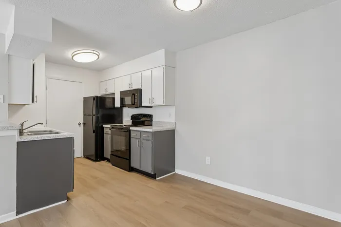 Modern kitchen with sleek black appliances, elegant white cabinetry, and stylish grey accents, featuring beautiful hardwood floors and ample natural light.