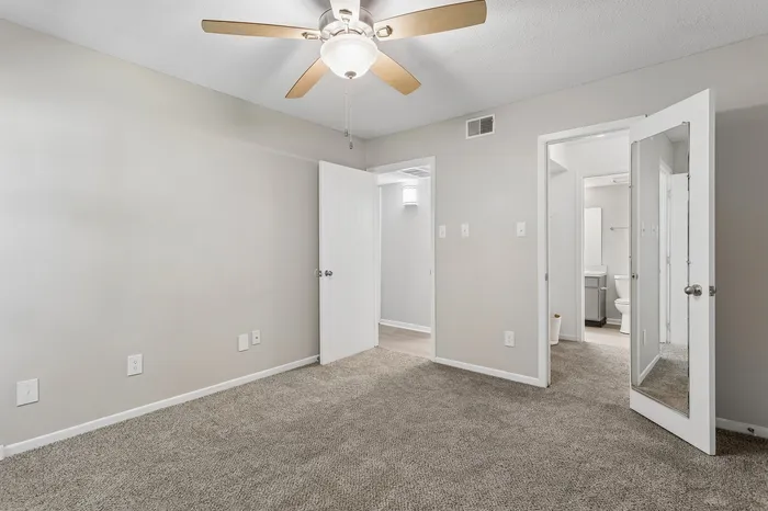 Bright bedroom featuring plush carpet, modern ceiling fan, and mirrored closet door.