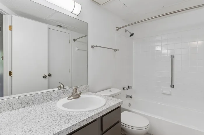 Contemporary bathroom featuring a sleek vanity with speckled countertop, large mirror, and pristine white tiling for a fresh, modern look.