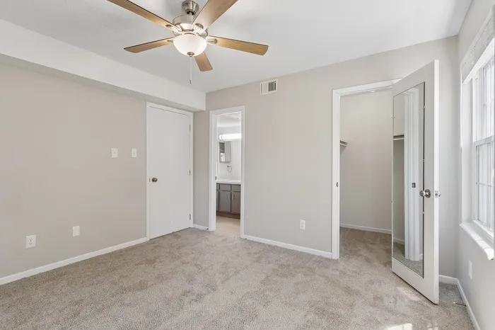 Bright and inviting room with plush carpet, ceiling fan, and ample natural light, offering access to a bathroom and spacious closet.