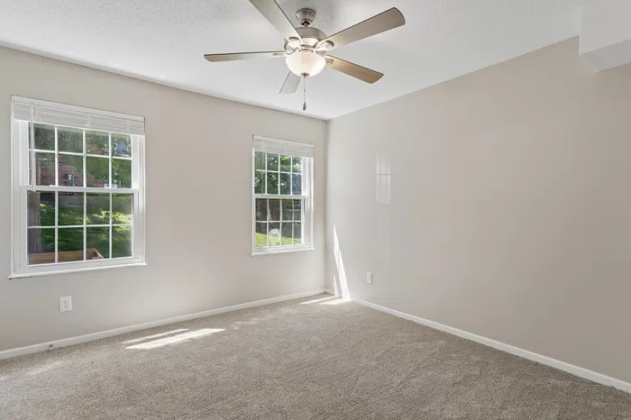 Bright and airy bedroom with plush carpeting, featuring large windows for natural light and a modern ceiling fan.